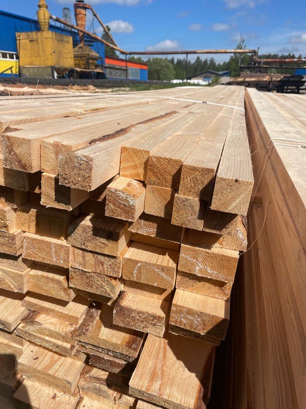 Squared timber packs stacked in the mill yard with production buildings behind